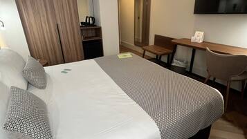 A hotel room with a large bed, a desk, a chair, a TV, and a mirror.