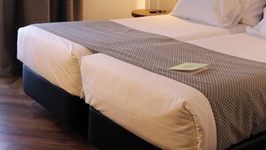 Una habitación de hotel con cama, mesita de noche, lámpara y cortina.