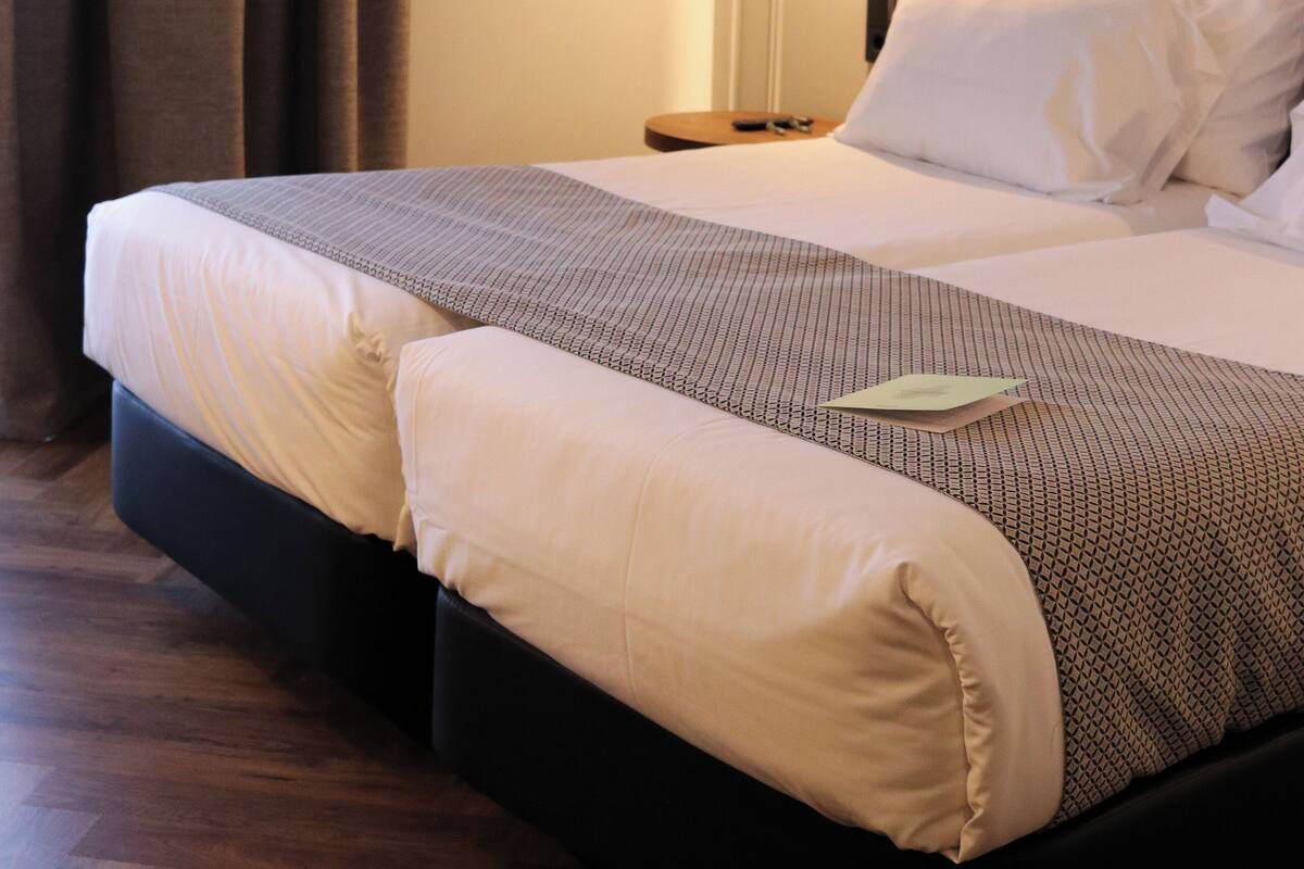 A hotel room with a bed, a nightstand, a lamp, and a curtain.