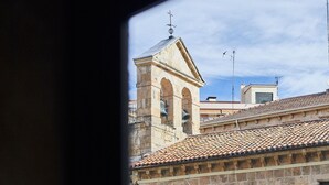 Vista a través de una ventana de un edificio de piedra con tejado de tejas y un campanario.