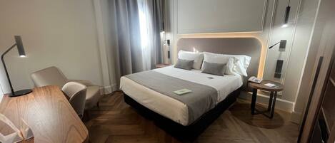 Una habitación de hotel moderna con una cama grande, un escritorio, una silla y una mesita de noche con lámpara.