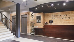 Zona de recepción de un hotel, con mostrador de recepción, un reloj y una escalera.