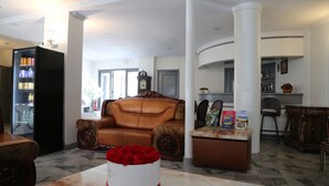 Un salon avec un canapé en cuir marron, une table blanche agrémentée d’un bouquet de roses rouges, et un réfrigérateur rempli de boissons.