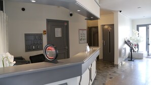 Un espace d’accueil comprenant un comptoir, une caméra de surveillance, une porte avec une pancarte et une affiche sur le mur.