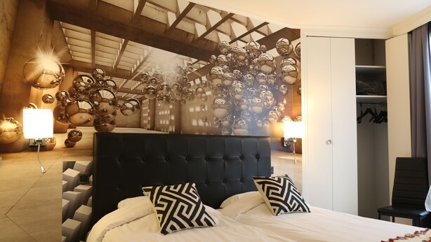 Une chambre d’hôtel moderne avec un grand lit, une tête de lit et un mur décoré de miroirs sphériques.