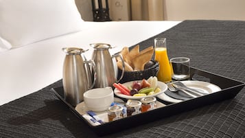 Bandeja de desayuno sobre una cama con colcha negra texturizada, que contiene croissants, una fuente de fruta, jugo, miel y una taza.