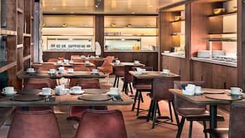 Een modern café met houten meubels, verschillende tafels en stoelen, en een zichtbare toonbank met een menukaart.