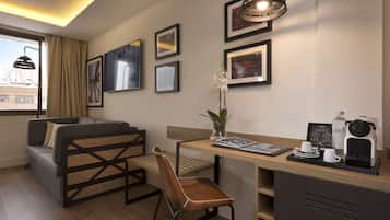A modern hotel room with a sofa, a wooden desk, a coffee machine, and framed pictures on the wall.