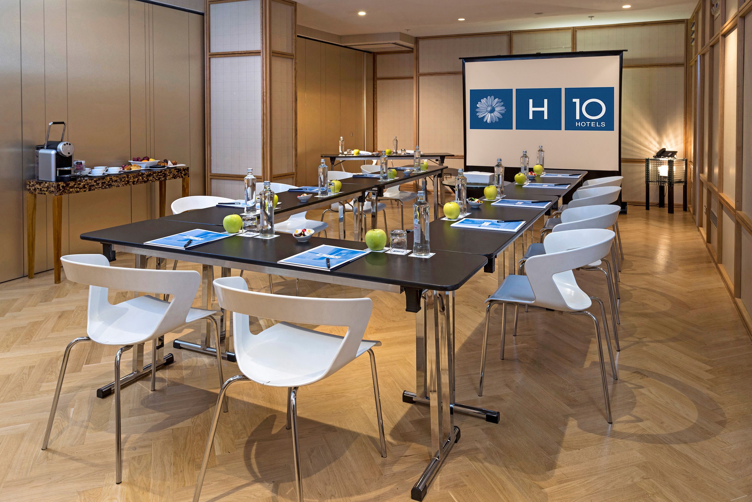 A conference room with a long table, white chairs, and a projector screen displaying the logo of a hotel chain.
