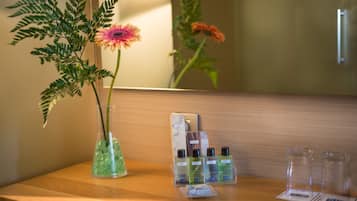 Un ripiano del bagno con un vaso di fiori, uno specchio e articoli da toilette.