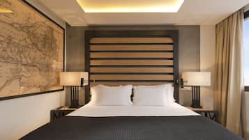 A neatly made bed with a dark quilt, two bedside lamps, a large framed map on the wall, and a modern headboard.