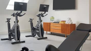 Un gimnasio en casa con dos bicicletas estáticas, una banca y mancuernas.