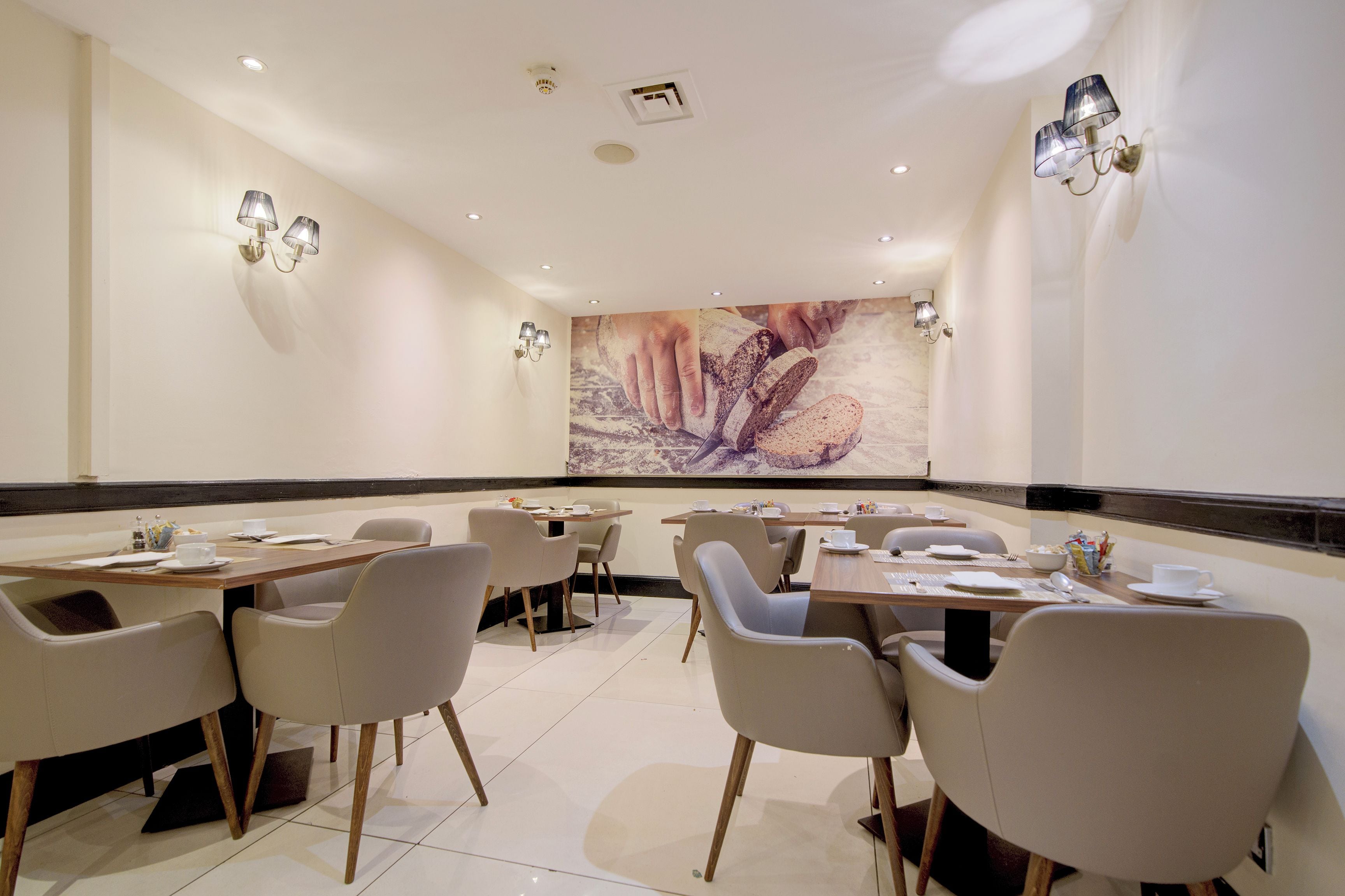 A modern dining area with multiple tables and chairs, recessed ceiling lights, and a large abstract painting on the wall.