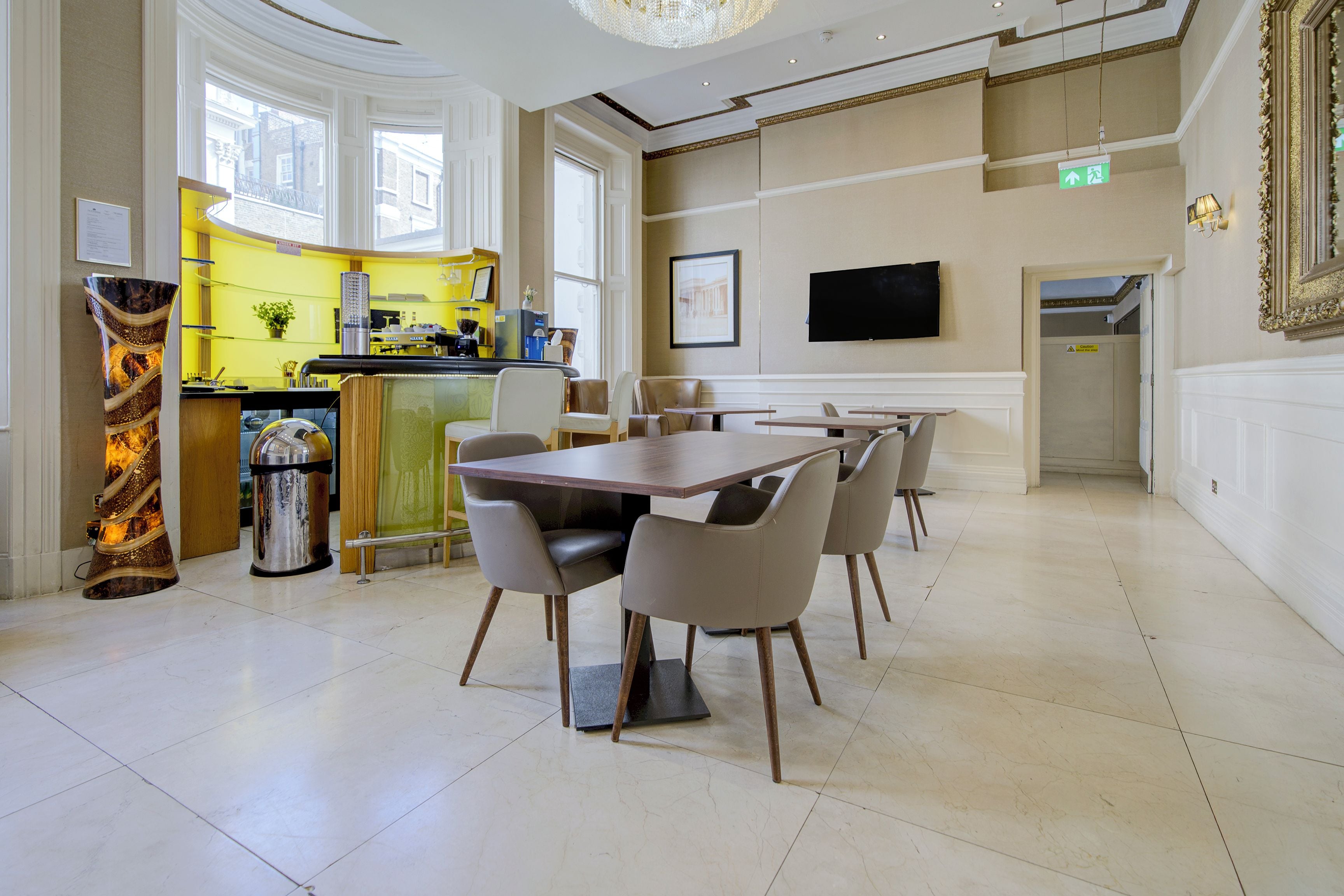 A hotel dining area with a bar, tables, chairs, and a television on the wall.