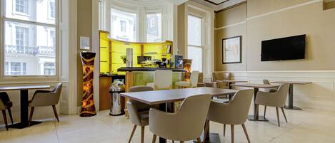 Un comedor moderno con una mesa grande y sillas, una cocina al fondo y un televisor montado en la pared.