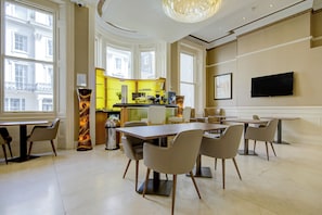 A modern dining area with a large table and chairs, a kitchen in the background, and a television mounted on the wall. - Sunday London Paddington Hotel (London)
