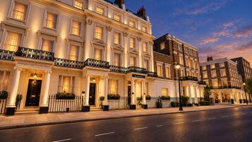 A row of traditional British townhouses with well-lit facades, a clear street, and a calm evening sky.