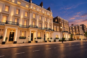 A row of traditional British townhouses with well-lit facades, a clear street, and a calm evening sky. - Sunday London Paddington Hotel (London)