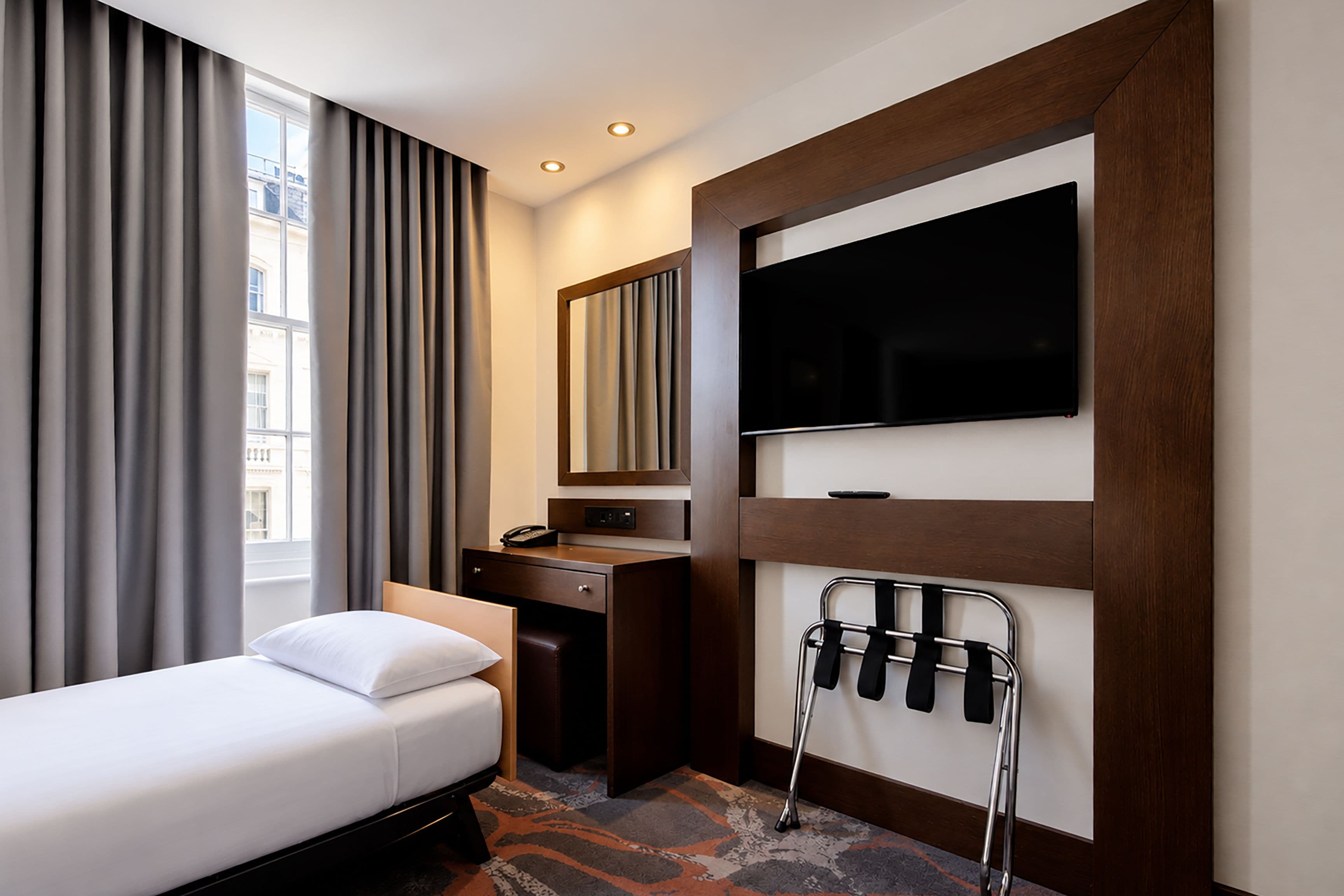 A hotel room with a bed, a desk, a chair, a TV, and a window with curtains.