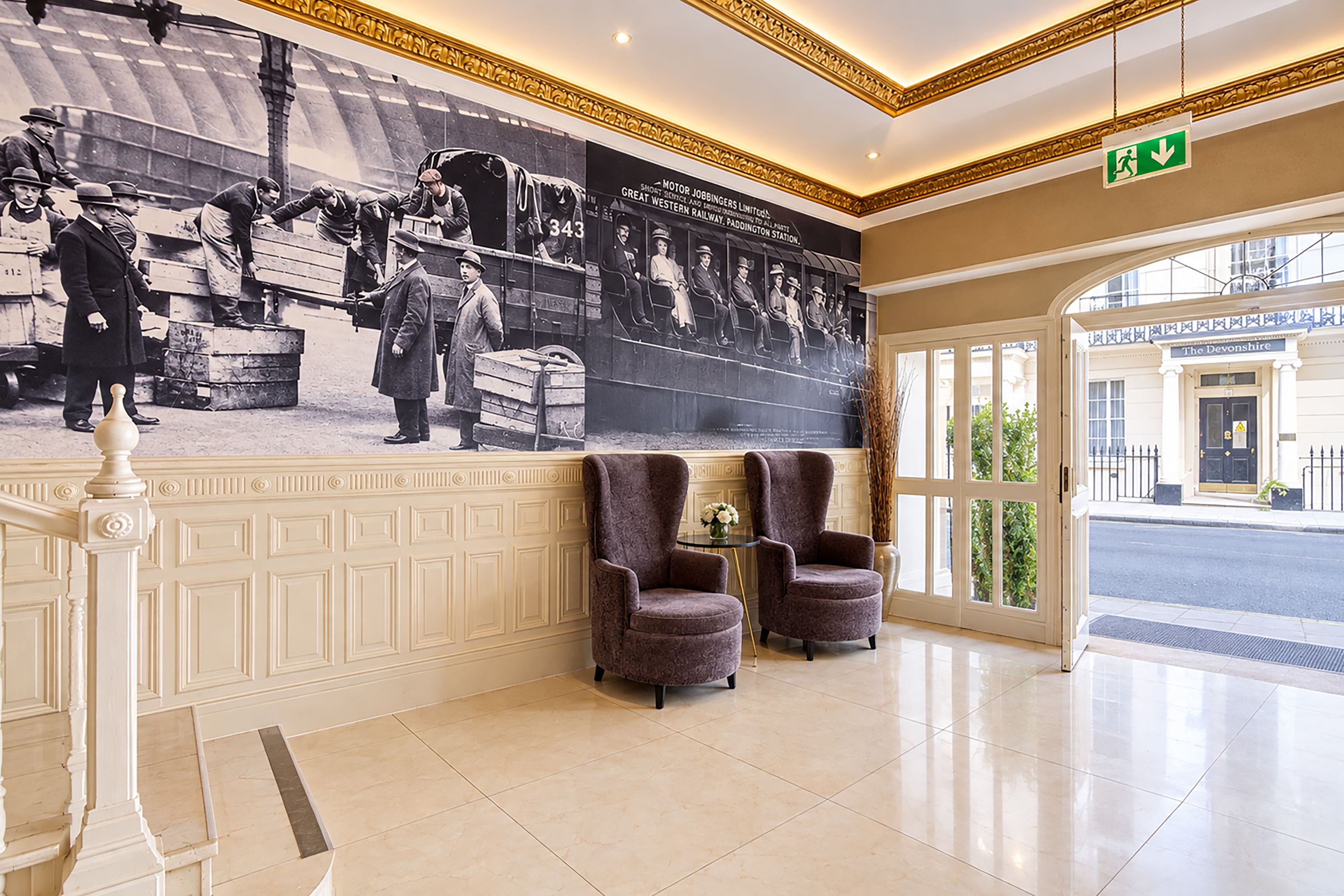 A lobby with a large historical photo mural, two armchairs, and a view of the street outside.