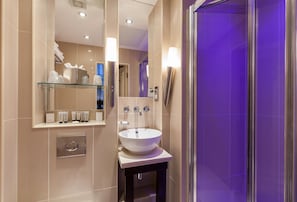 A modern bathroom with a large mirror, a white sink, and a glass shelf with toiletries.