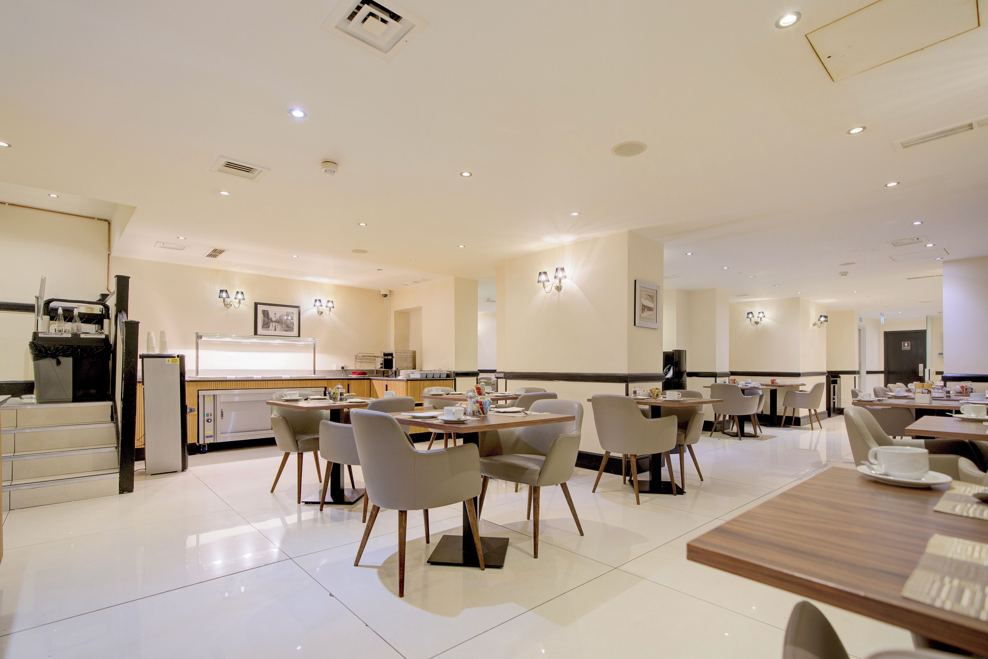 Un espace repas moderne avec des tables et des chaises, un coin cuisine et un comptoir avec un réfrigérateur.
