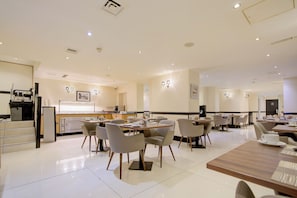 A modern dining area with tables and chairs, a kitchen area, and a counter with a refrigerator. - Sunday London Paddington Hotel (London)