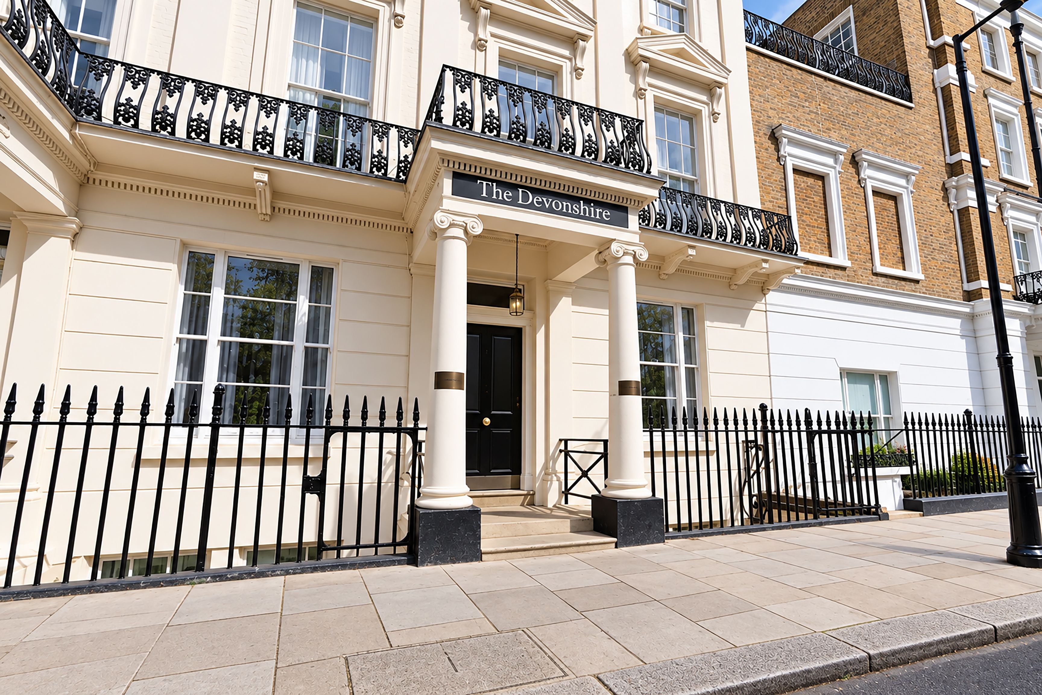 A building with a sign reading 'The Devonshire' above the entrance, featuring a classical architectural style with columns and a black iron fence.