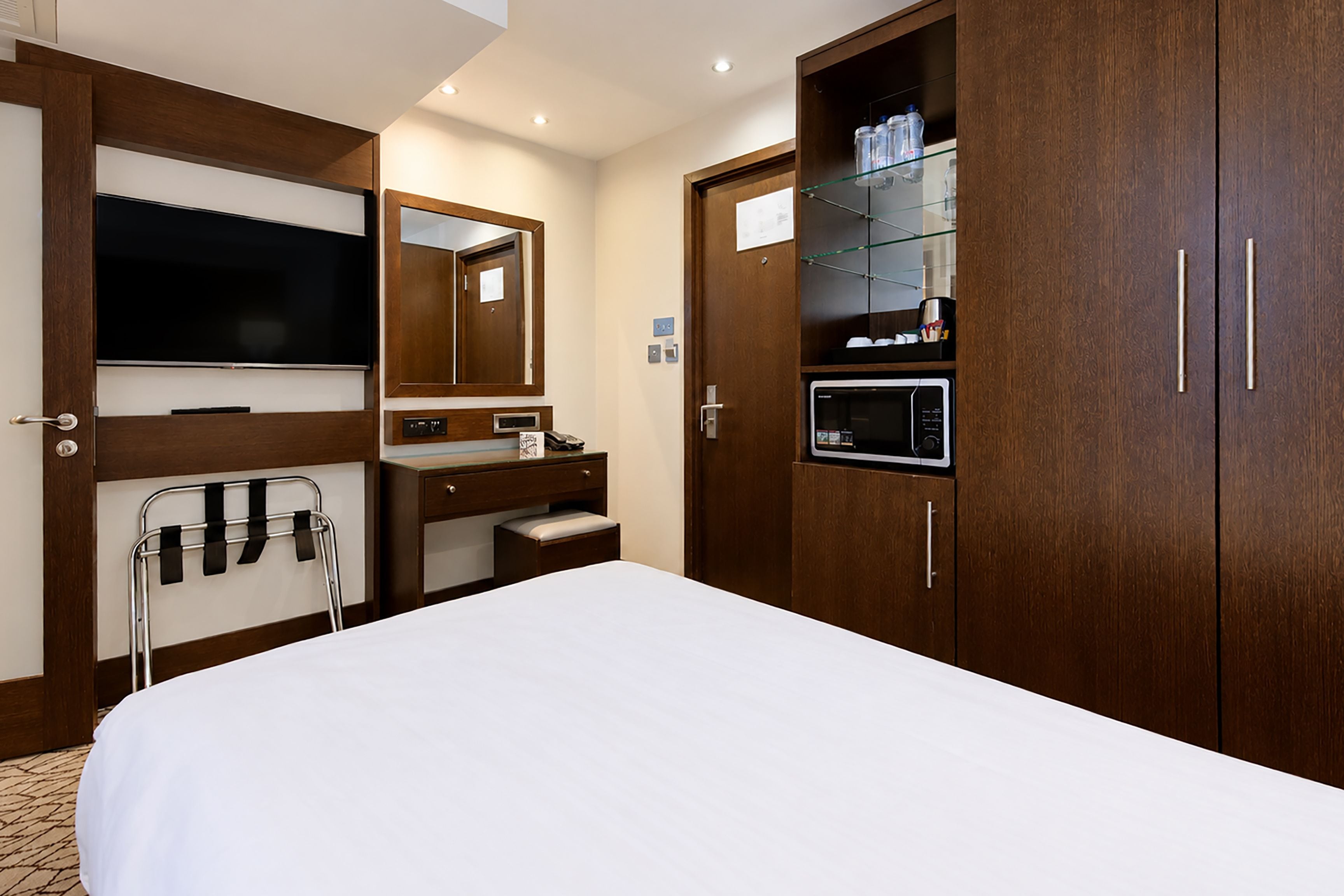 Una camera d'albergo con un letto, una TV, uno specchio, un lavabo con mobile e un armadio.