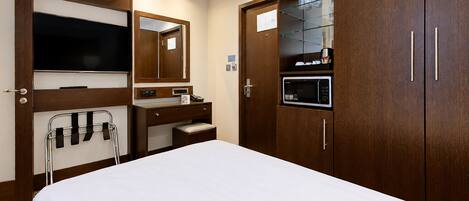 Una camera d'albergo con un letto, una TV, uno specchio, un lavabo con mobile e un armadio.