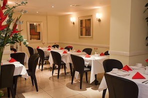 A dining area with multiple tables and chairs, each set with white tablecloths and red napkins. - Sunday London Paddington Hotel (London)