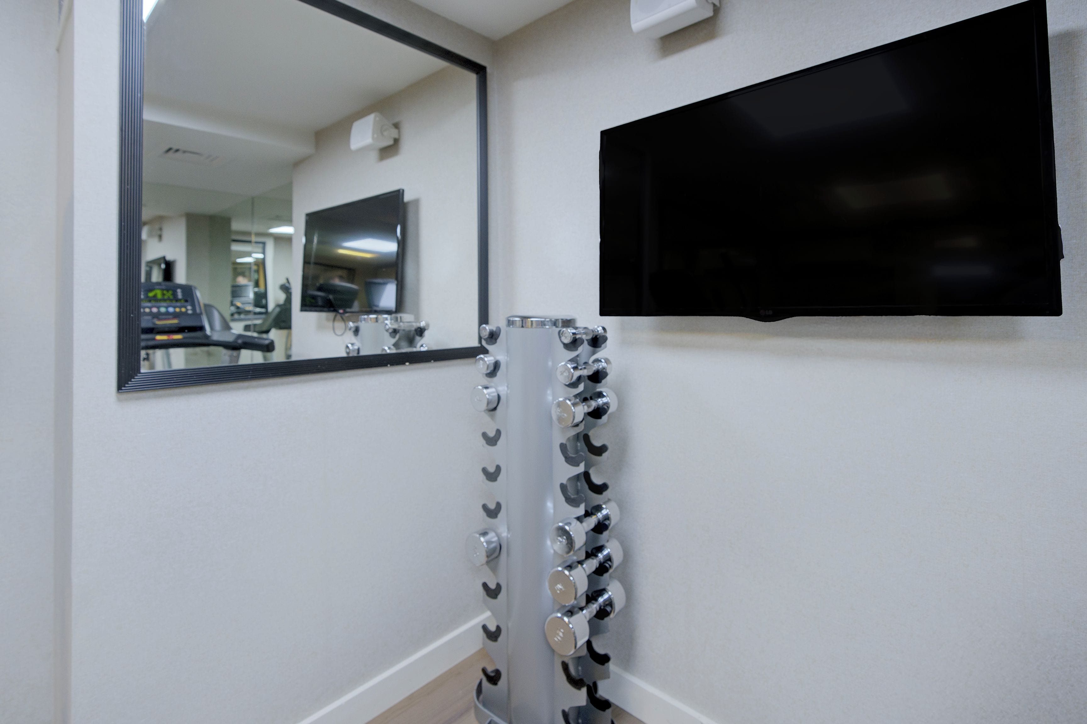 A bathroom with a mirror, a wall-mounted TV, and a rack of dumbbells.