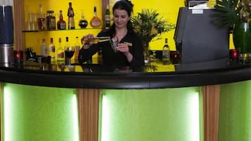 A bar area with a bartender preparing a drink, shelves with various bottles, and a decorative plant.