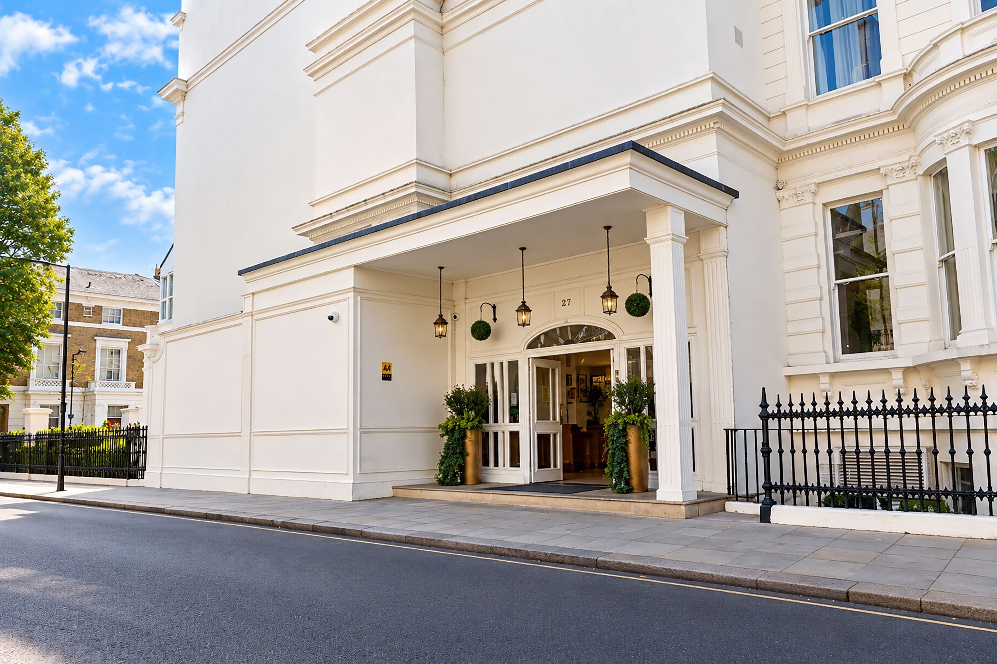 A white building with a classic architectural style, featuring a prominent entrance with a covered porch and a black wrought iron fence.