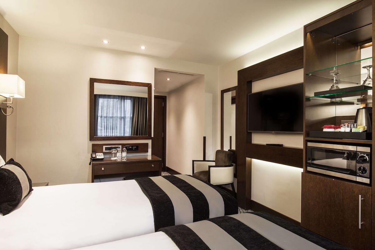 A hotel room with two beds, a desk with a telephone, a television, a microwave, and a minibar.