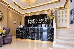 A reception desk with a black marble top, a sign reading 'Park Grand Paddington Court,' and a staircase to the right. - Sunday London Paddington Hotel (London)
