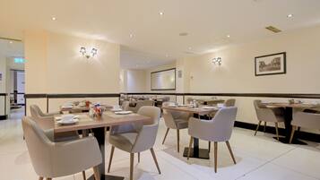 A hotel dining area with tables, chairs, and wall-mounted lighting.