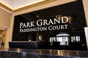 A reception area with a black marble counter and a sign that reads 'PARK GRAND PADDINGTON COURT'. - Sunday London Paddington Hotel (London)