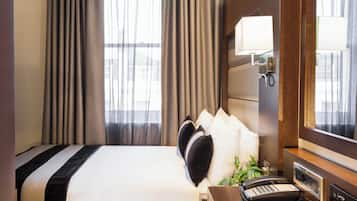 A hotel room with a large bed, a bedside table with a phone and a book, a mirror, and curtains.