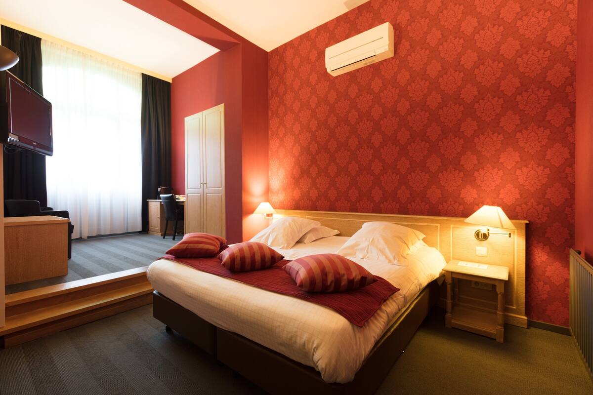 A hotel room with a large bed, bedside tables, a desk, and a television.