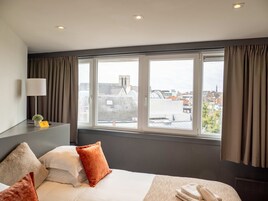 Habitación de hotel con un ventanal grande, una cama con almohadas, una mesita de noche con una lámpara y un cartel que indica prohibido fumar.