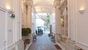 A corridor with ornate ceiling and columns, potted plants, and benches. - Hotel Gravensteen (Ghent)