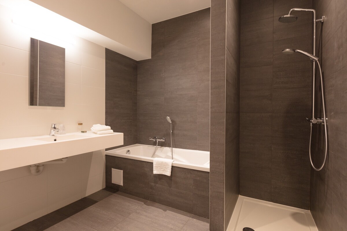 Un baño moderno con un tocador blanco, una bañera y una zona de ducha.