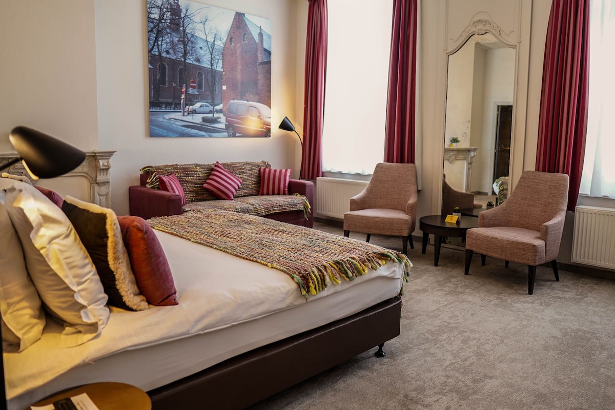 A hotel room with a large bed, two armchairs, a small table, and a painting on the wall.