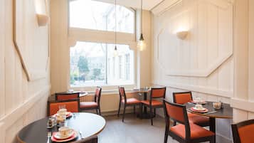 Un comedor con mesas redondas y sillas naranjas, ventanas amplias y vistas a edificios.