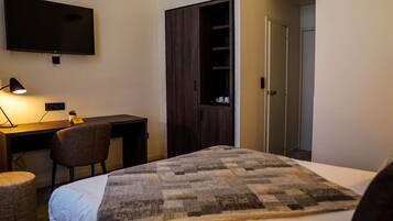 Habitación de hotel con cama, escritorio con silla, televisor montado en la pared y armario.