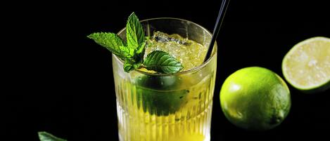A glass of yellow beverage with mint leaves and a lime half, against a black background.