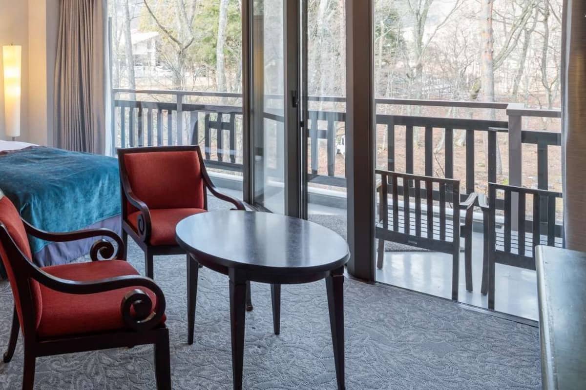 A hotel room with two beds, a small table, two chairs, and a balcony with a railing.