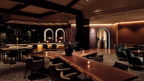 Un área de bar moderna con mesas de madera, taburetes y una iluminación ambiental.