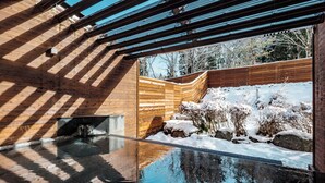 Un edificio moderno con fachada de madera, un estanque reflectante y un paisaje nevado visible a través de un espacio abierto.